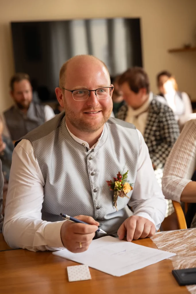 Authentisches Bild von Bräutigam wie dieser bei der standesamtlichen Hochzeit unterschreibt. Natürliche Hochzeitsfotos, heiraten in Tiefenbach