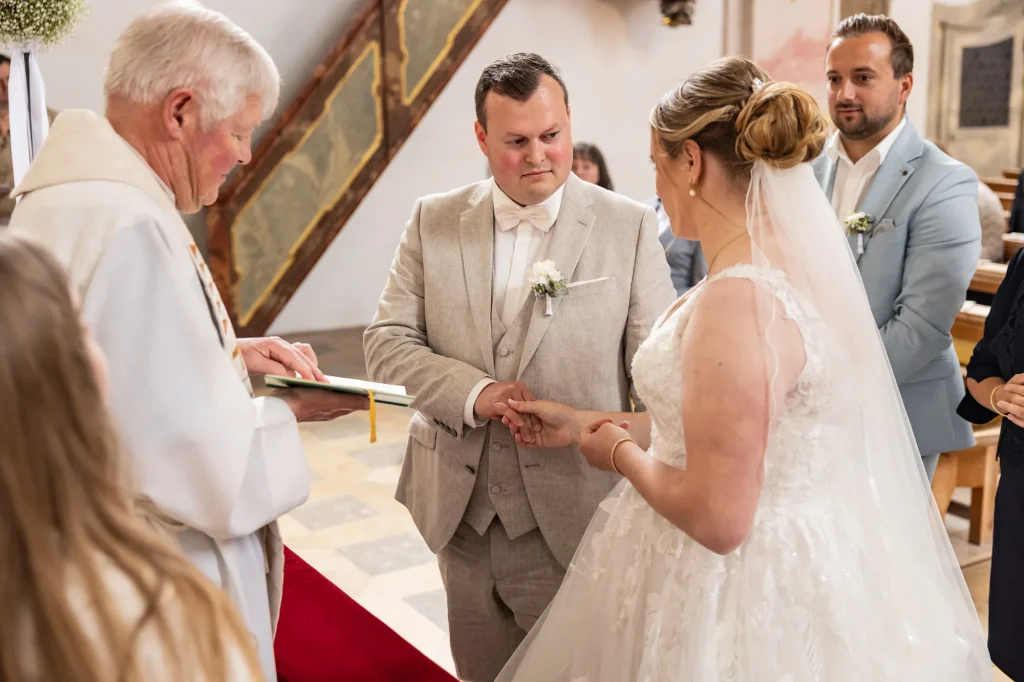 Sehr schönes Bild von glücklichen Brautpaar. Braut steckt Hochzeitsring ihren Bräutigam an den Finger. Heiraten in Neukirchen vorm Wald