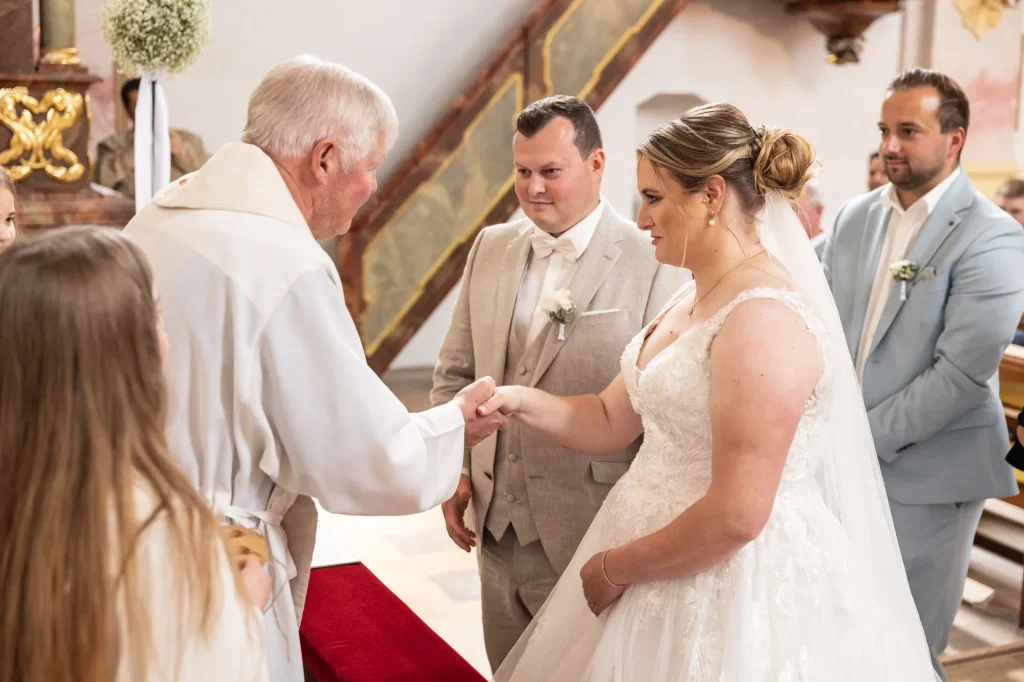 Wunderschönes Foto von Brautpaar während kirchlicher Trauung mit Pfarrer. Heiraten in Neukirchen vorm Wald