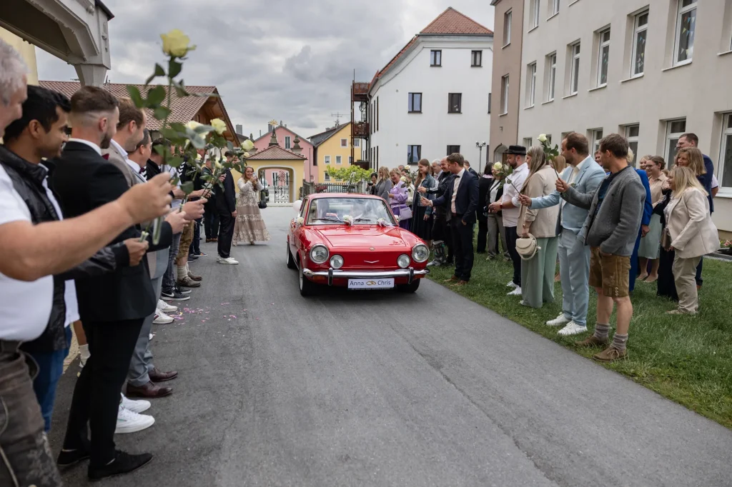 Sehr schönes Bild von Brautpaar im roten Hochzeitsauto nach kirchlicher Trauung in Neukirchen vorm Wald