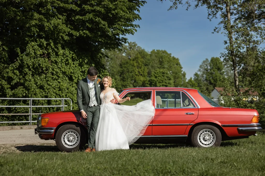 Dieses schöne Bild zeigt das Brautpaar mit deren wunderschönen Hochzeitsauto - einen schönen roten Mercedes. Hochzeitsreprotage von Daniela Schmid Fotografie