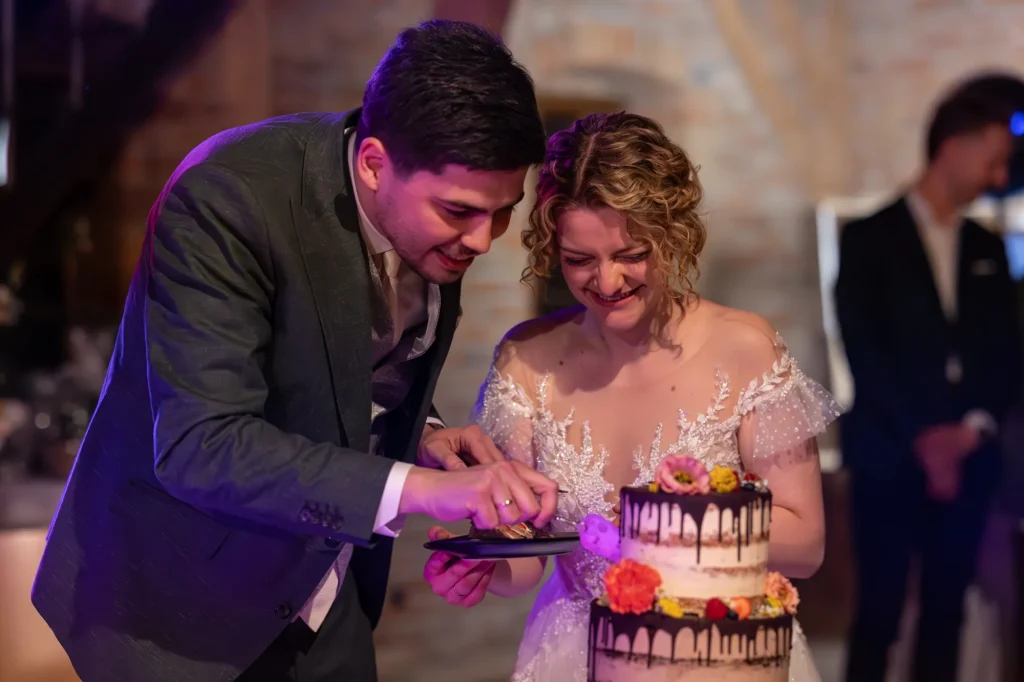 Wunderschönes Bild von Brautpaar beim Anschnitt der Hochzeitstorte bei ausgelassener Feier am Rahaberghof im Bezirk Schärding. Sehr schönes ungestelltes Bild von Daniela Schmid Fotografie